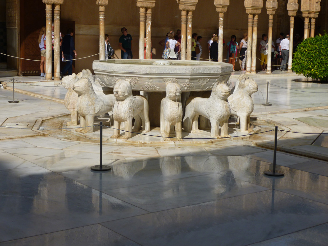 A fountain basin surrounded by stylised lions.  The lions go all the way around, from this angle, you can see either of them.  In the background are arches and a lot of tourists.