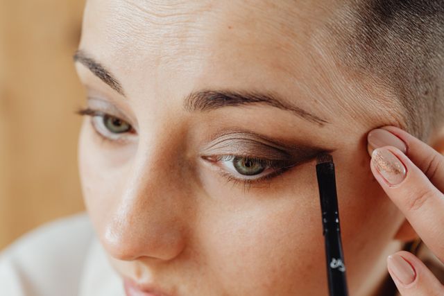 simple way to apply eyeliner as a beginner, woman using eye pencil and smudging with a brush for simple and soft eyeliner look 