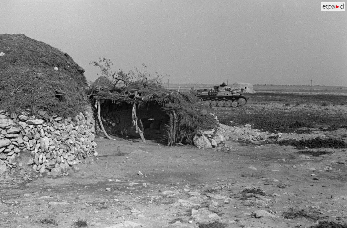 Panzer II (Pz-II) passent près d'une habitation de pierre et de paille.
