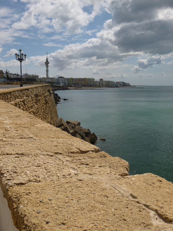 Seafront brick wall with old fashioned street lamps.  This runs along the left of the photo. The top right is the sky and the bottom right is the sea.