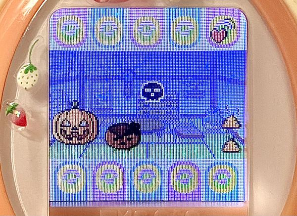 close up image of a tamagotchi device. the screen shows a crying, dirty sakuramotchi in a dark room with her own feces and a festive jack o lantern