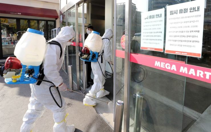 Karyawan pusat kesehatan umum memasuki pusat perbelanjaan skala besar di Distrik Dongnae Busan pada 22 Februari untuk mengasapi di dalam tempat yang ditutup pada hari itu. Pusat perbelanjaan itu adalah tempat seorang pria berusia 19 tahun mengunjungi sebelum dipastikan telah terinfeksi virus corona baru. 