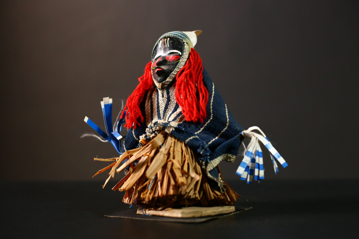 Front view of African ritual doll with red yarn and raffia skirt