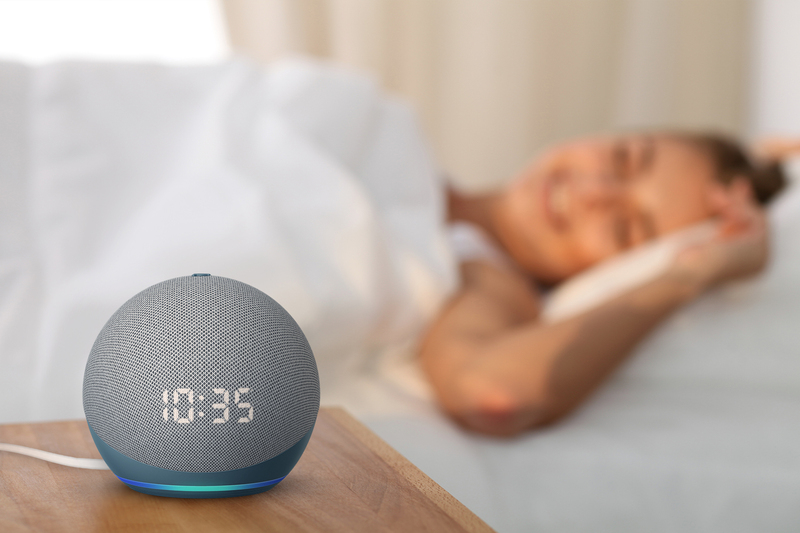 A imagem mostra uma pessoa deitada na cama e em cima da mesa uma Amazon Echodot 4ª geração com relógio