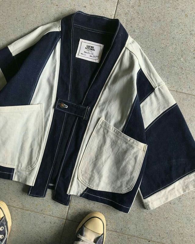 Blue robot-like figure with red shoes on a wooden platform with lights, on a white background