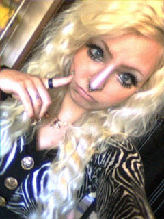 close up selfie of Ray with finger touching cheek. long wavy blonde hair with thick makeup and nude lips.