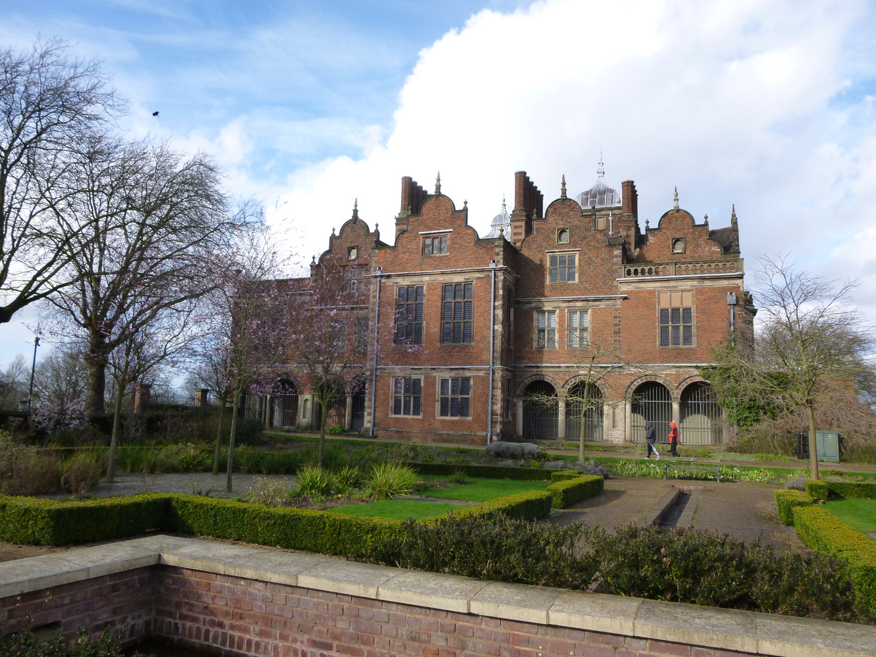 Another photo of the hall, this time from the left hand side. This side is also made of bricks. There are four sort of clover shaped roofs, repeating patterns very much a thing. In front of the house is a small garden. The trees are bare because it was March.