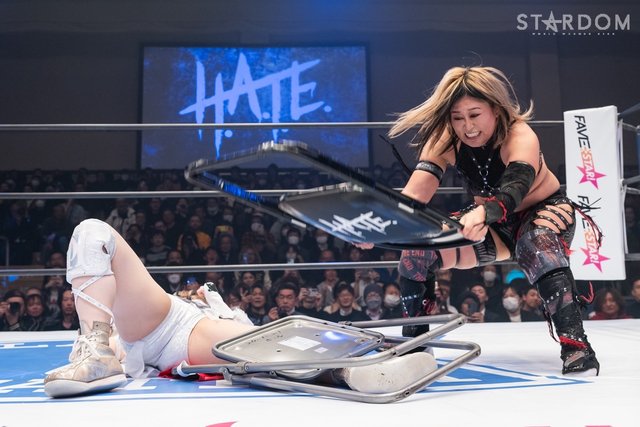 Photo from STARDOM of Konami hitting Natsupoi's leg with a chair which is already wrapped with another chair.
