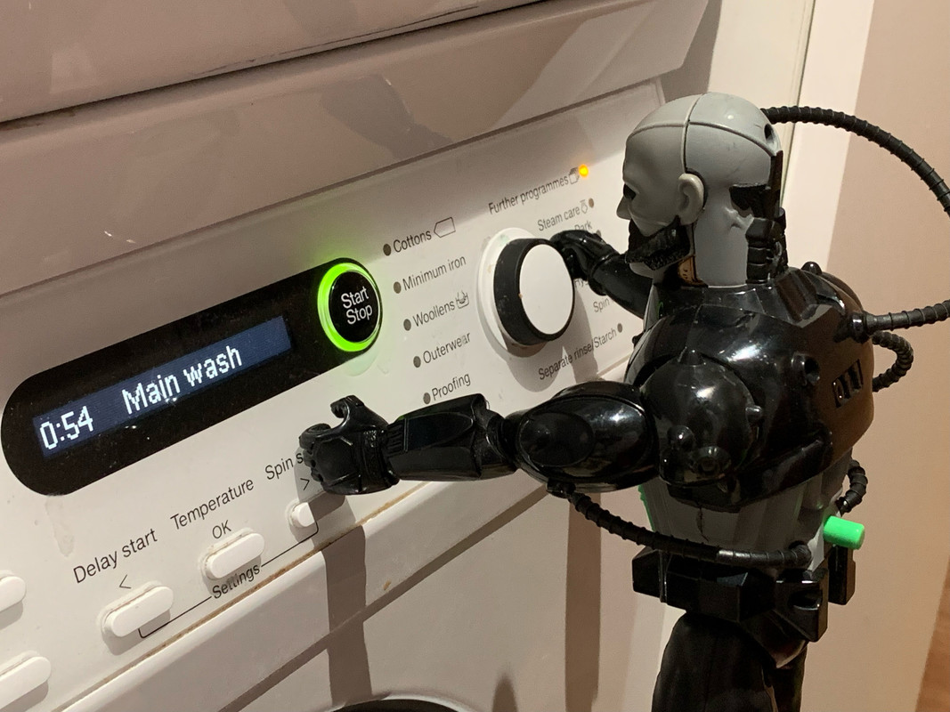 Black robot helping to Load in the dirty clothes into the washing machine. 7-D2-CD7-C7-5606-4135-9932-C97840770-B46