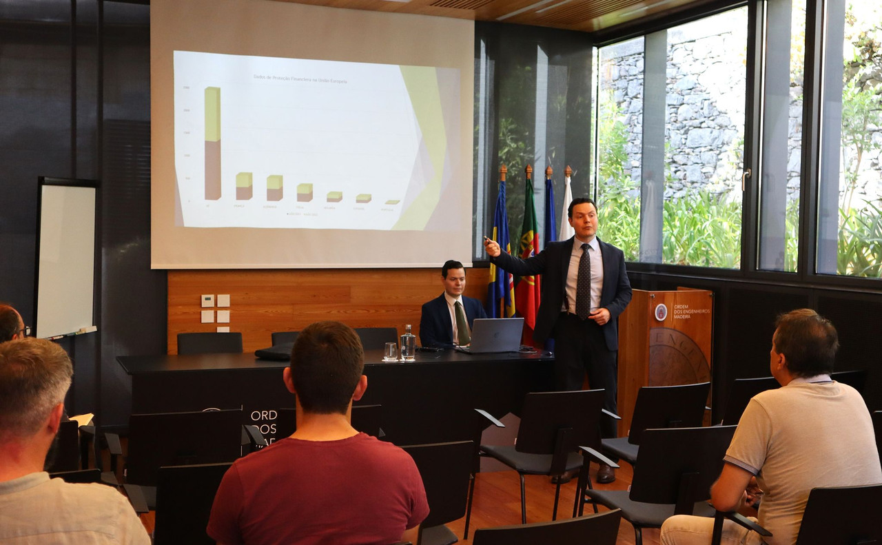 José e Luis Rafaschieri em conferência financeira, apresentando gráficos sobre proteção de investimentos na Europa, com bandeiras e público atento.