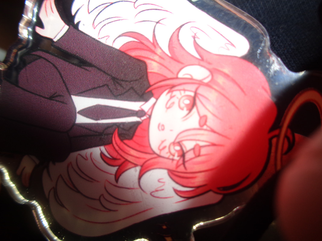 A very closeup photo of an angel devil keychain. Angel devil is a long-haired, suit-wearing, winged character.