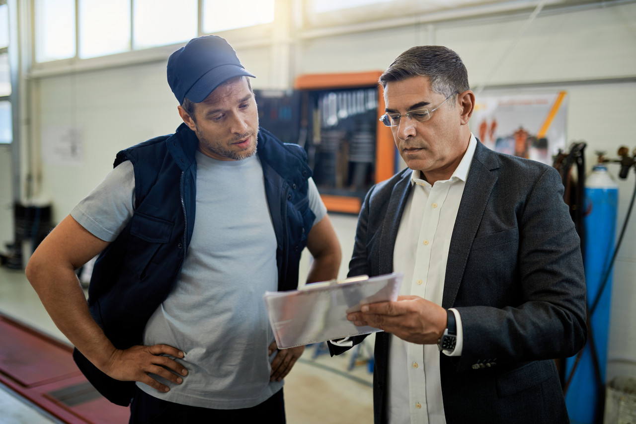Mid Adult Manager Car Mechanic Analyzing Data While Going Trough Reports Auto Repair Shop