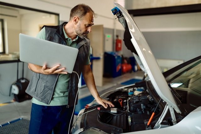 The Importance of Regular Car Battery Maintenance Auto-repairman-using-laptop-while-examining-car-engine-workshop-min-Easy-Resize-com