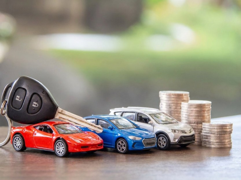 car key beside miniature cars and stacks of coins on a table