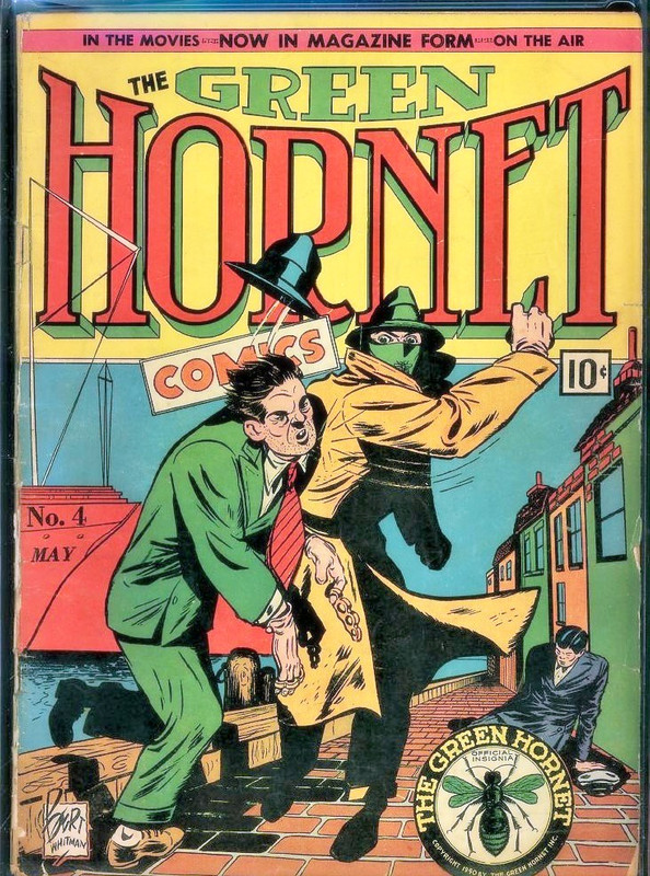 Cover image from the Green Hornet comic book series, The Green Hornet is punching out a bad guy and another bad guy lies slumped in the background. They are on a dock and there is a cargo ship in the background. The bad guy getting punched is wearing brass knuckles and his hat has been knocked into the air by the punch.
