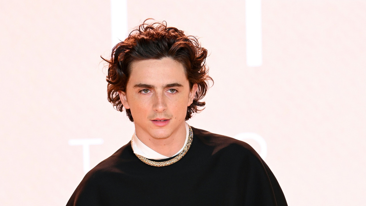 Timothée Chalamet smiling in a white suit with silver jewelry
