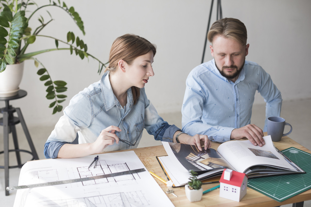 professional male female architect looking catalog while working office