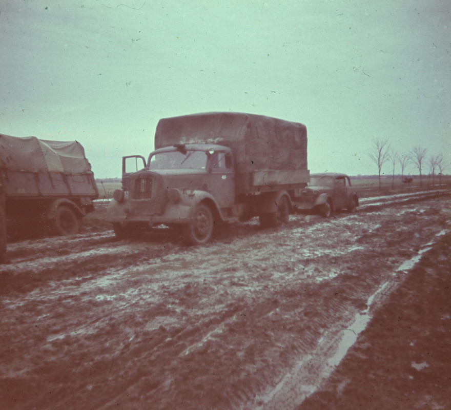 Drei Militärfahrzeuge fahren einen schlammigen Weg entlang.