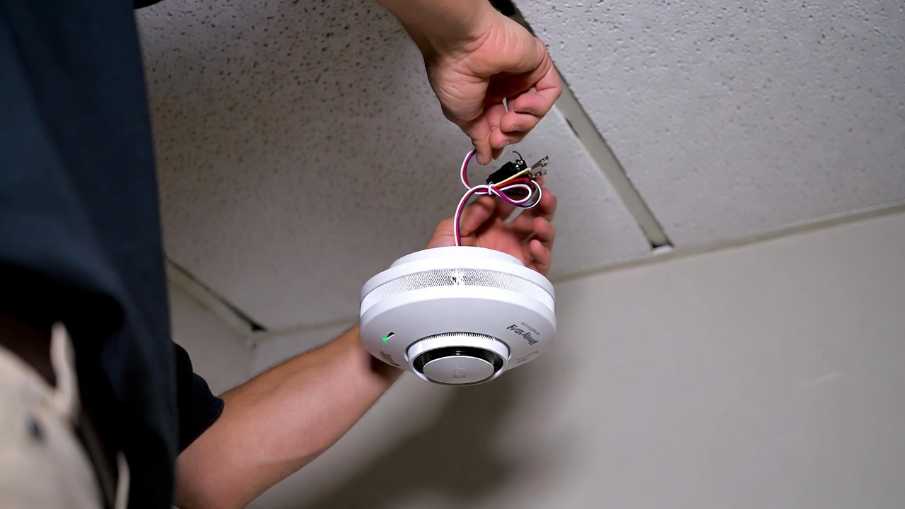 Person installing First Alert Onelink Smart Smoke Detector with wire connections visible