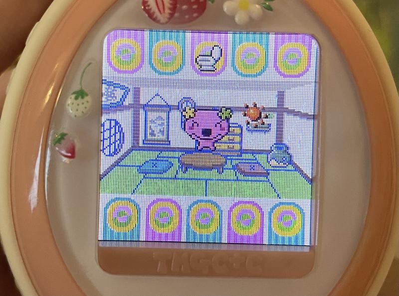 close up photograph of a tamagotchi plus color device. furawatchi is smiling and jumping up in the air happily