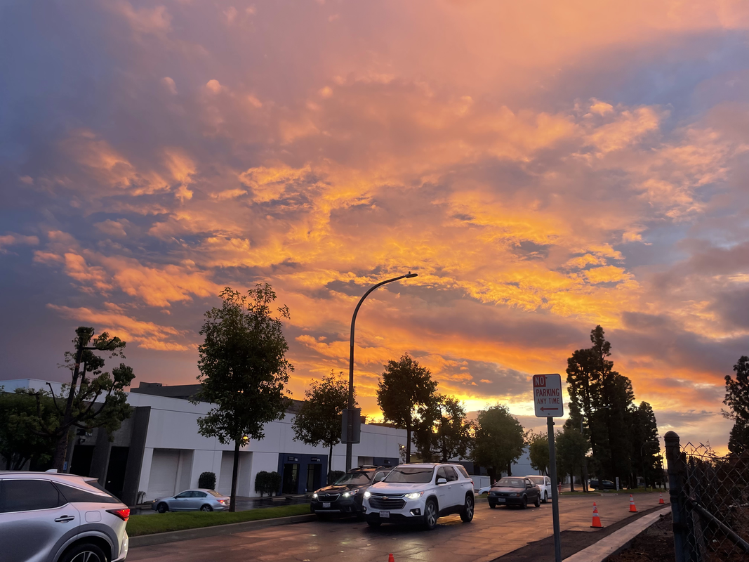 A photo of a very intense sunset-- with a lot of orange and ssomme purple/yellows as it bleeds into the blue sky behind it. A sort of suburban street is in front of it.