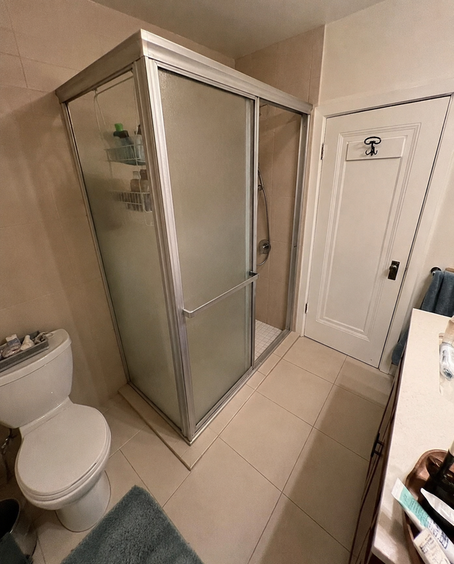 Guest bathroom before — framed sliding shower door, beige ceramic tile, chrome hardware