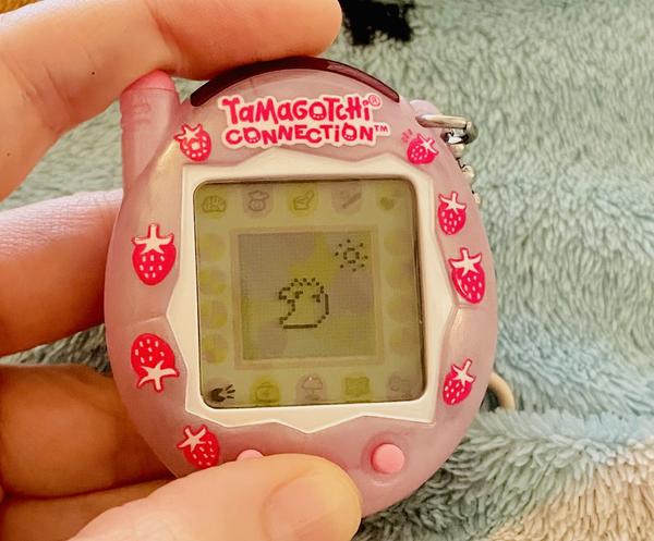 up close photo of a tamagotchi connection device (2024 rerelease) showing ALIBI leaping up happily and smiling