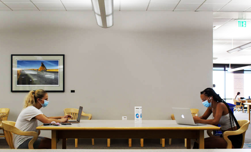 Two students sitting across from each other at a table and wearing face masks.