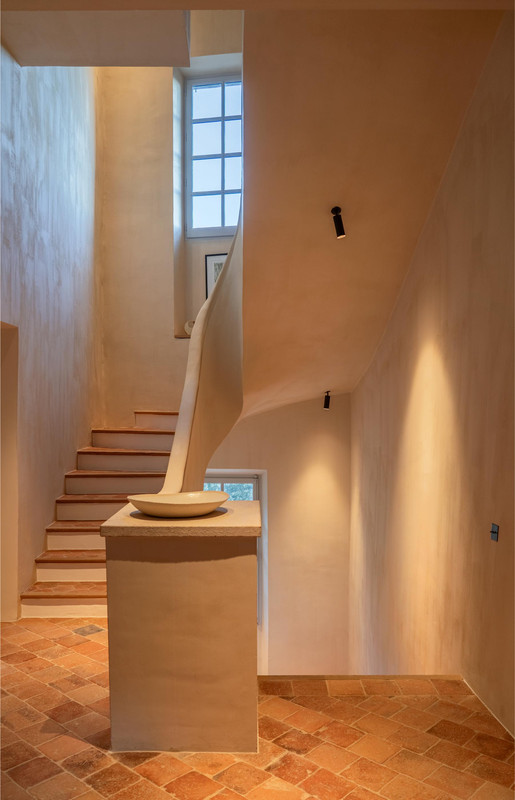 Luxuriöse Treppenbeleuchtung in Château Bénat mit fokussierter Wandbeleuchtung, minimalen Deckenleuchten und warmem Terrakottaboden