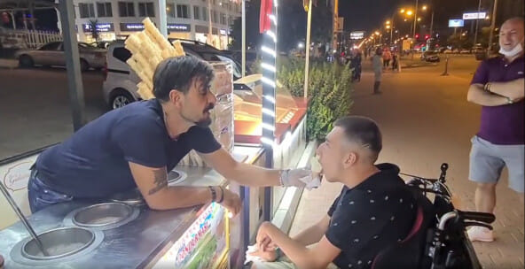 Penjual menyuapi pria berkursi roda dengan es krim
