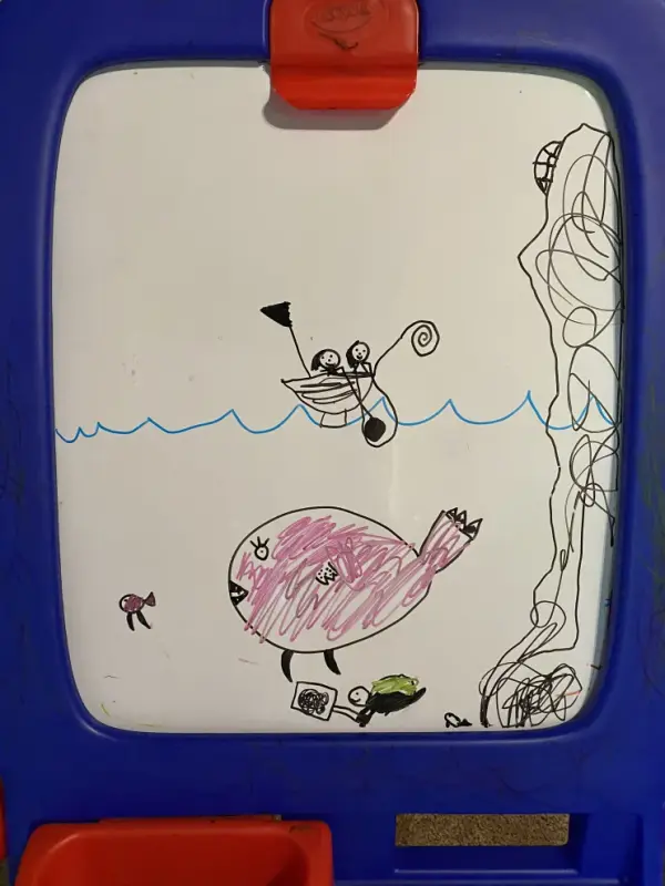whiteboard art featuring two figures in a boat and a very large, pink fish underneath them in the ocean. The pink fish has eyelashes. There is also a sea turtle and what appears to be a cliff to the right. It is clearly drawn by a young child.