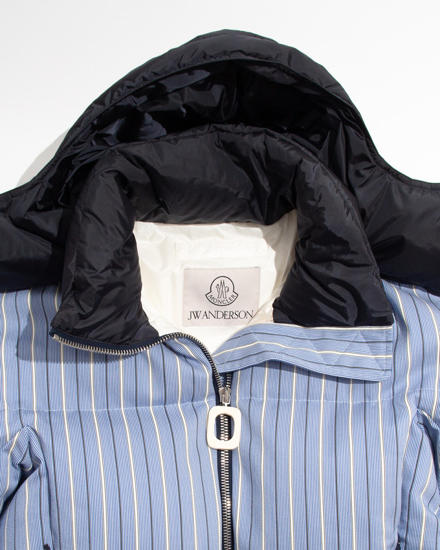 Moncler x JW Anderson FW25 – Dettaglio piumino a righe blu e bianche Dettaglio del piumino a righe blu e bianche Moncler x JW Anderson FW25 con cappuccio nero e logo ricamato