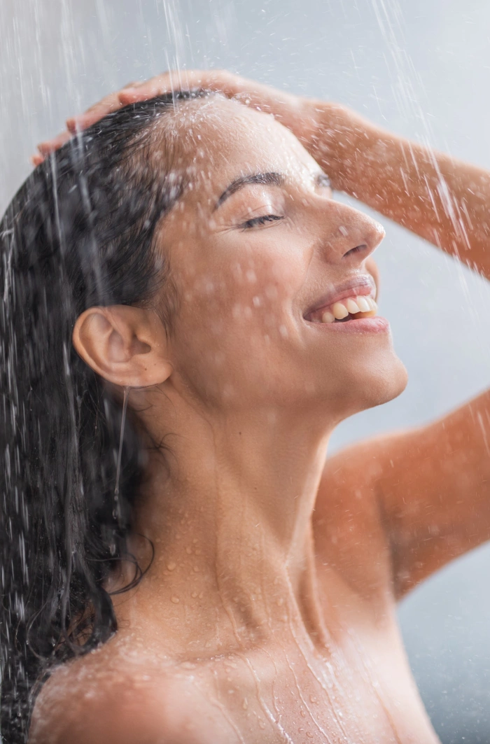A smiling girl washes her hair with only water in the shower