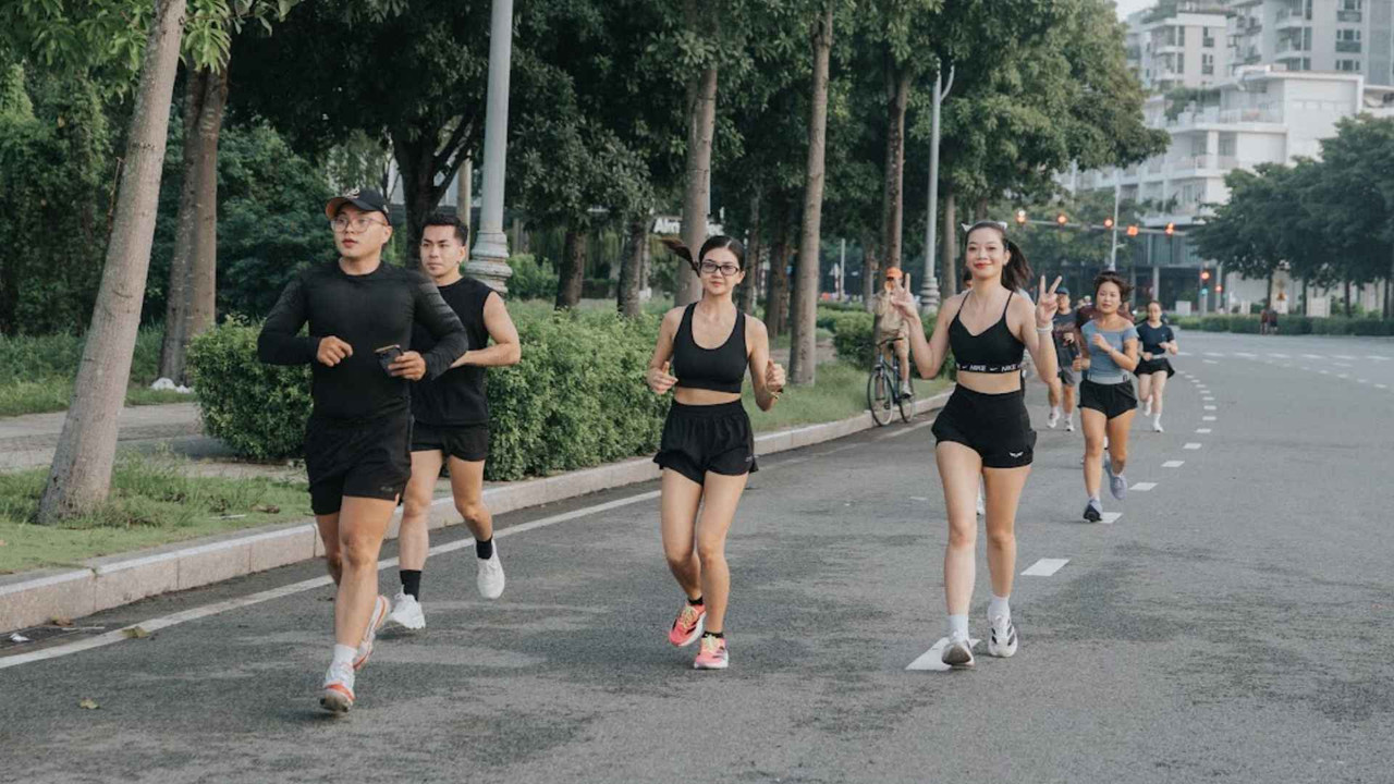 Nhóm chạy bộ cười nói thoải mái, tạo dấu hiệu tay vui vẻ khi đang chạy trên đường