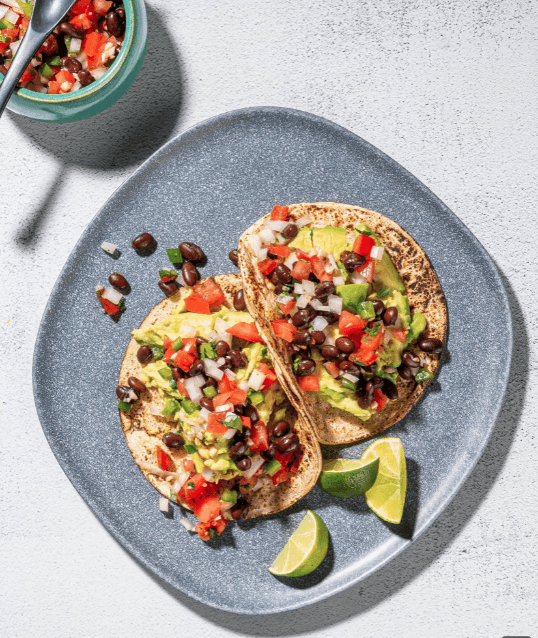 two avocado tacos with slices of limes on a grey plate