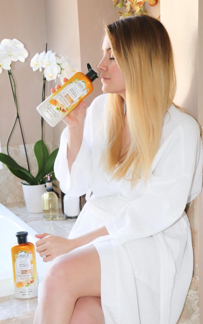 Blonde woman smells shampoo sitting by the bathtub