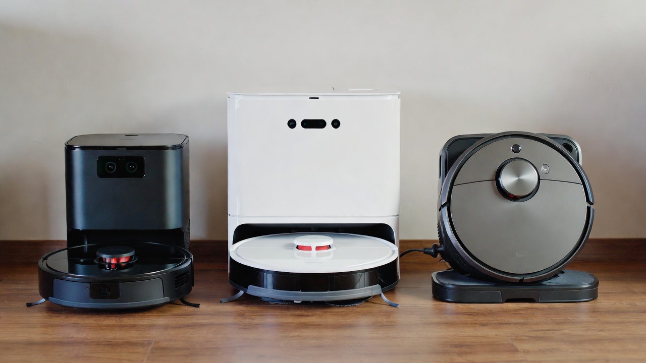 Three different robot vacuums lined up on hardwood floor showing size differences