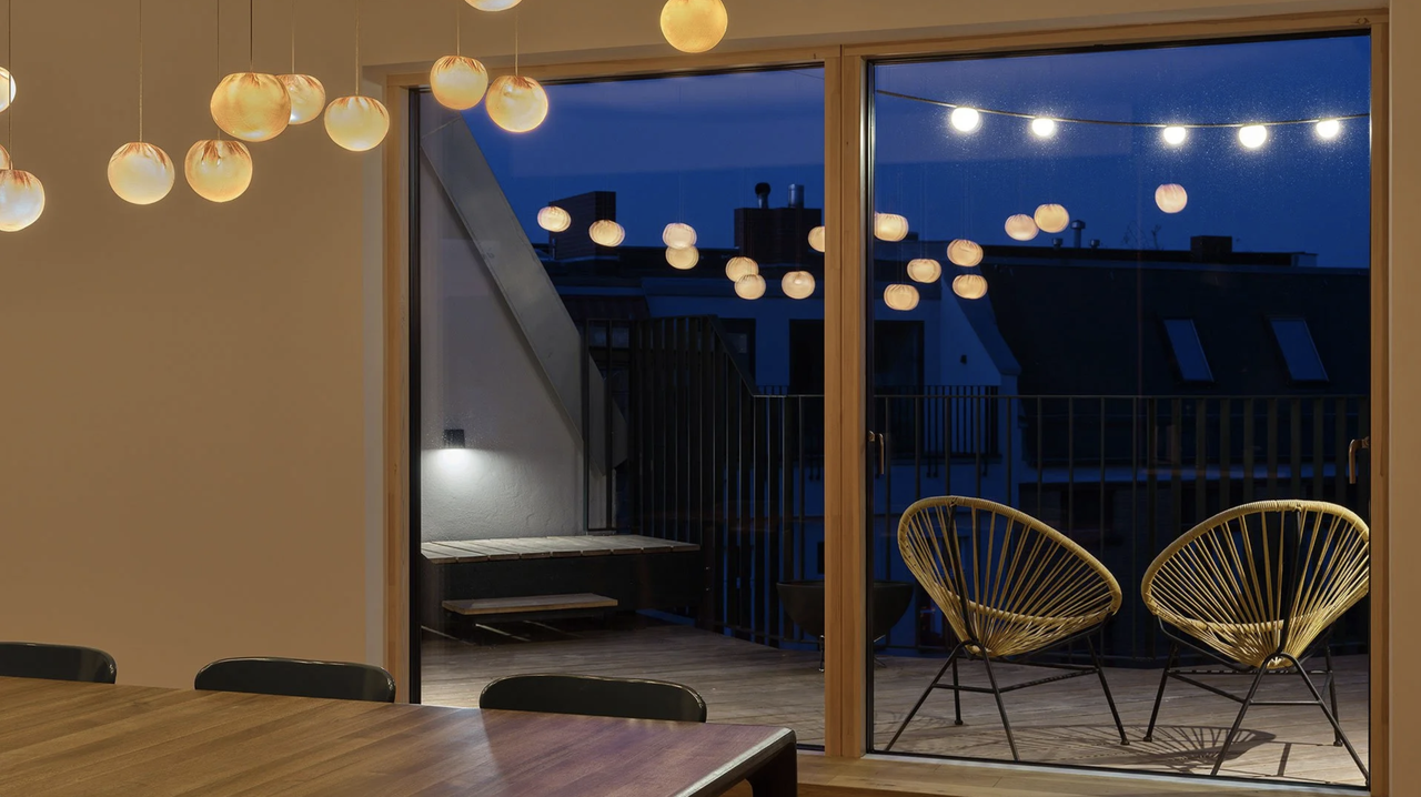 Beleuchtete Dachterrasse der Privatwohnung Inselstraße mit Sitzbereich, Wandleuchte und Lichtkette