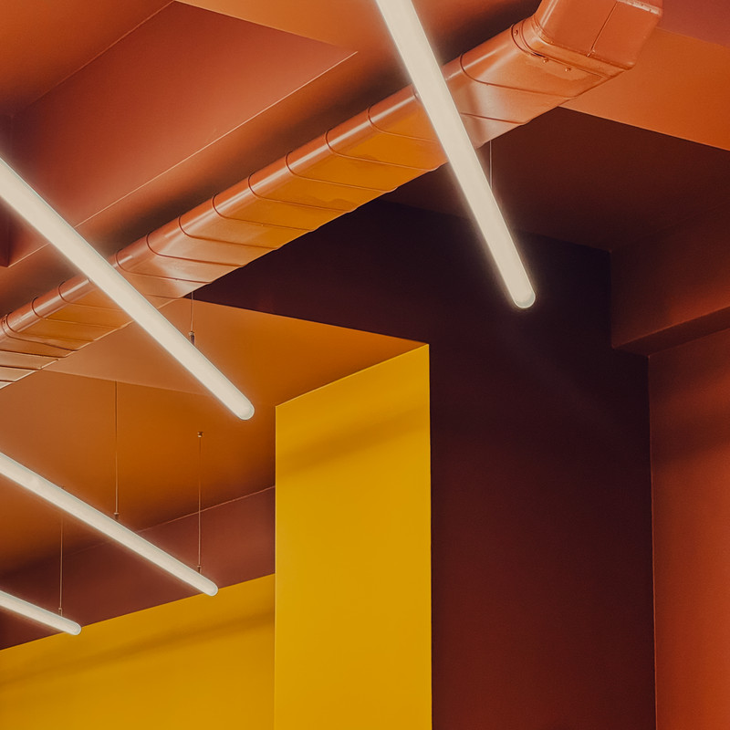 Detail der linearen Leuchten bei Flip-N-Fry im Zusammenspiel mit orangefarbenen und gelben Architekturflächen