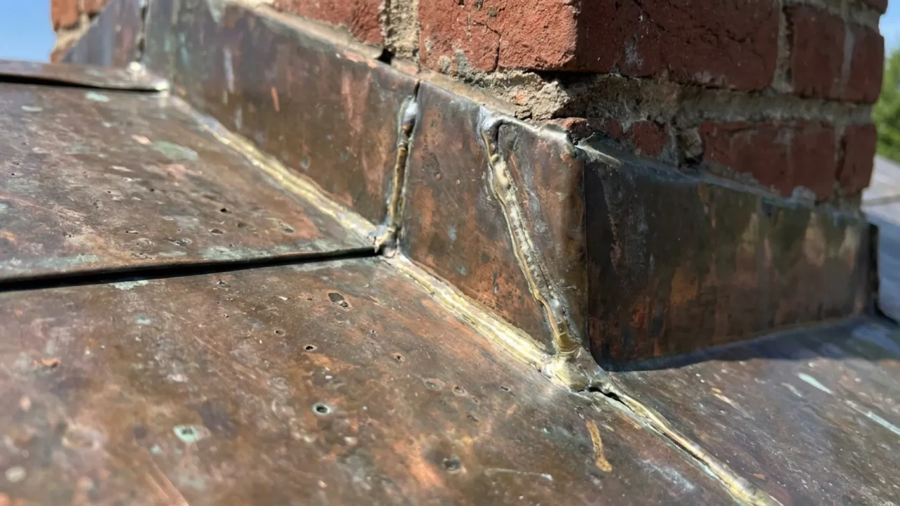Detail view of copper roof flashing at chimney penetration on a San Antonio home showing soldered seam joints and proper copper-to-copper connection