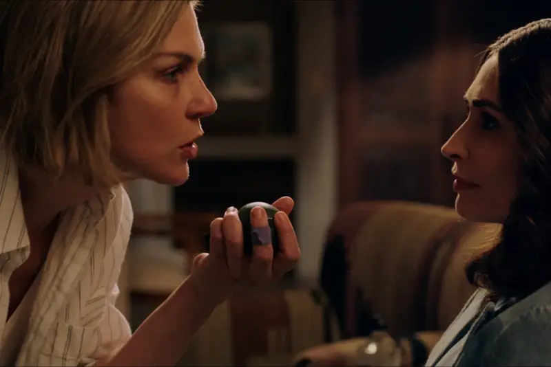still frame from pluribus showing Carol speaking to zosia while holding a hand grenade