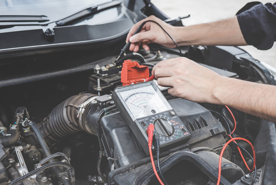 Mechanic uses multimeter to test car electrical circuit in engine bay