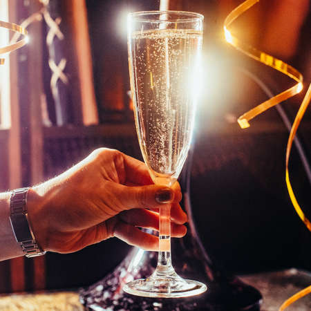 98838605-party-and-holiday-celebration-concept-glass-with-champagne-in-hand-toned-image-with-festive.jpg