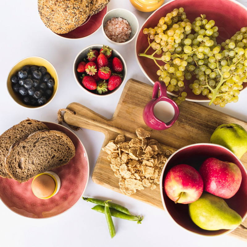 Colazione ricca di frutta e vitamine per mantenere il colorito della pelle Una tavola imbandita con una colazione salutare: frutta come fragole, mirtilli e uva, cereali, pane integrale e uova. I cibi sono ricchi di vitamine essenziali per la salute della pelle e il mantenimento dell'abbronzatura