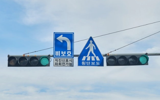 Korean unprotected left turn (biboho) sign mounted on a traffic signal with a green light and crosswalk sign