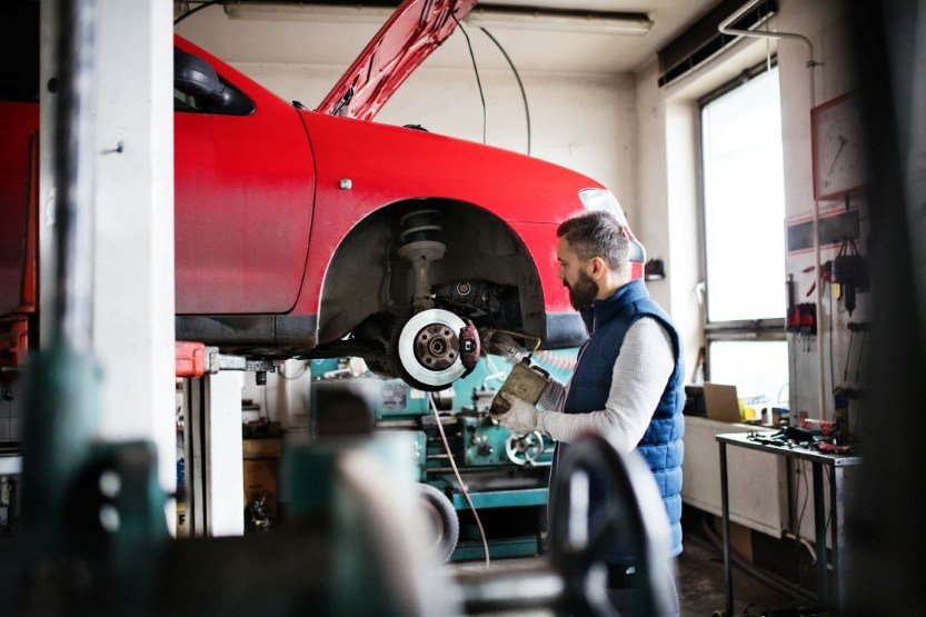 mechanic inspecting the suspension and brake components of a raised vehicle in an auto repair shop