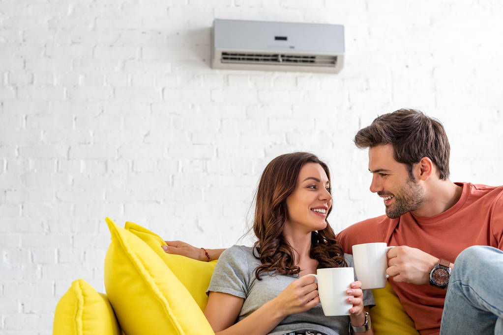 Couple sitting on sofa under air conditioner