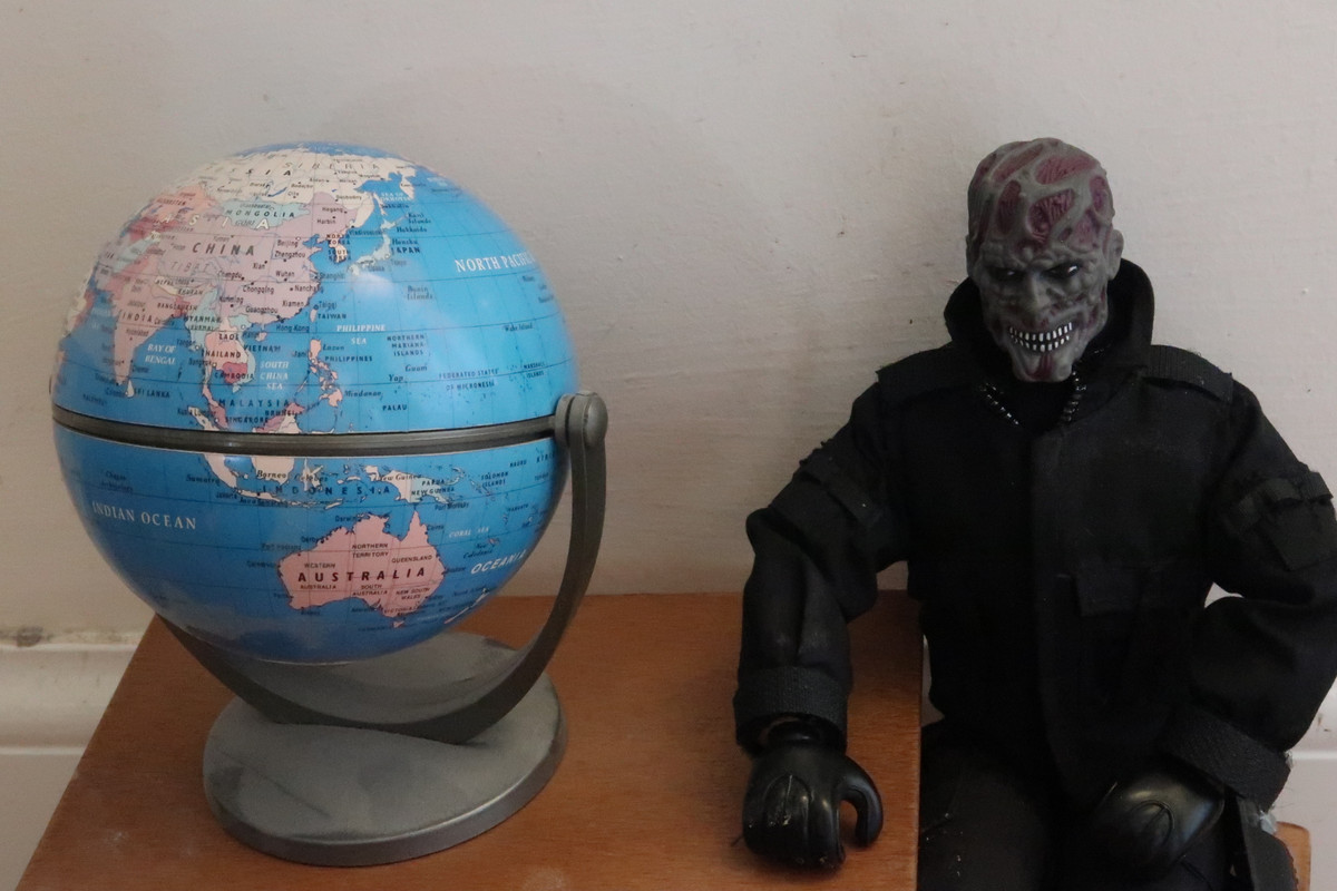 No Face sitting on a stool beside a table and a globe of the world.  A3-FD284-D-3281-45-B0-A4-DC-BBB0-DF85314-C