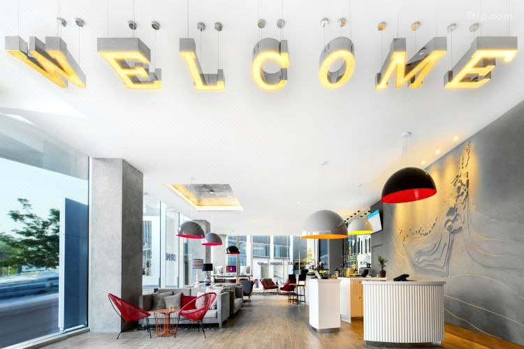 القاعة الرئيسية لفندق Ibis Styles Dubai Airport Hotel مع كلمة "Welcome" مكتوبة في السقف.
