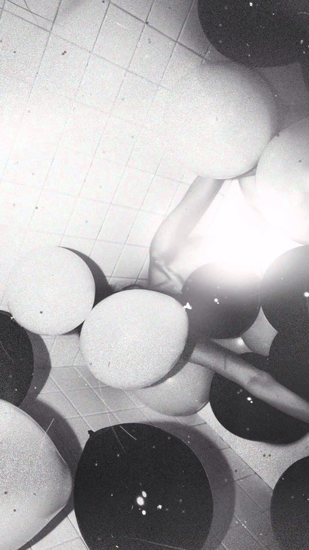 A grainy, black and white photo of a person amidst balloons in a bathtub.